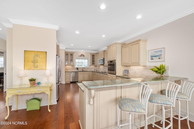 kitchen with appliances with stainless steel finishes, a breakfast bar, dark hardwood / wood-style flooring, ornamental molding, and kitchen peninsula