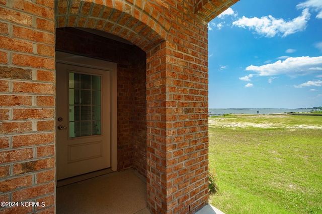 doorway to property with a lawn and a water view