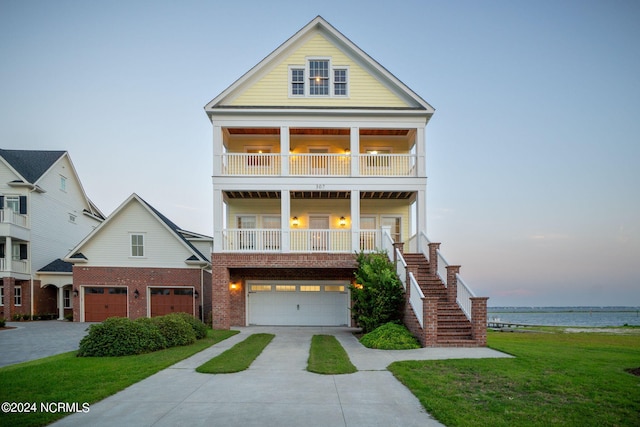 view of front facade with a balcony, covered porch, a lawn, a garage, and a water view