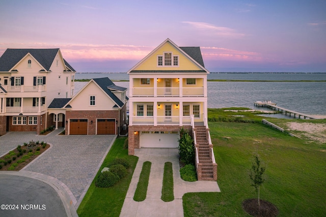 view of front of property featuring covered porch, a garage, a balcony, and a water view