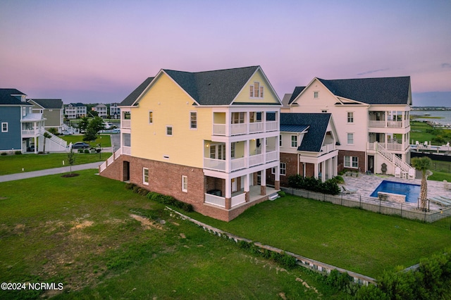 back house at dusk featuring a balcony and a yard