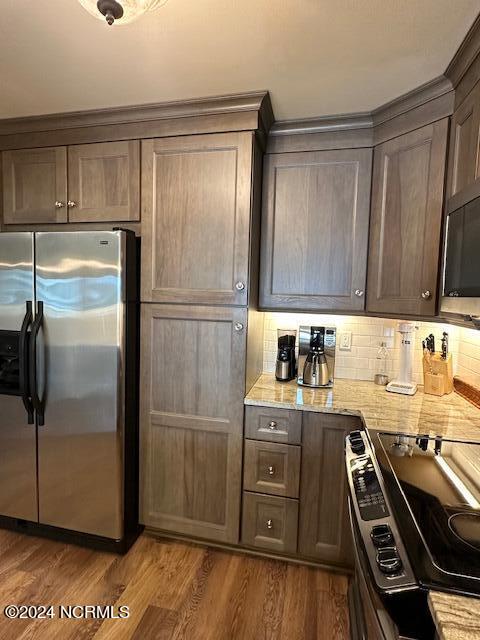 kitchen featuring hardwood / wood-style floors, electric range, decorative backsplash, light stone counters, and stainless steel refrigerator with ice dispenser