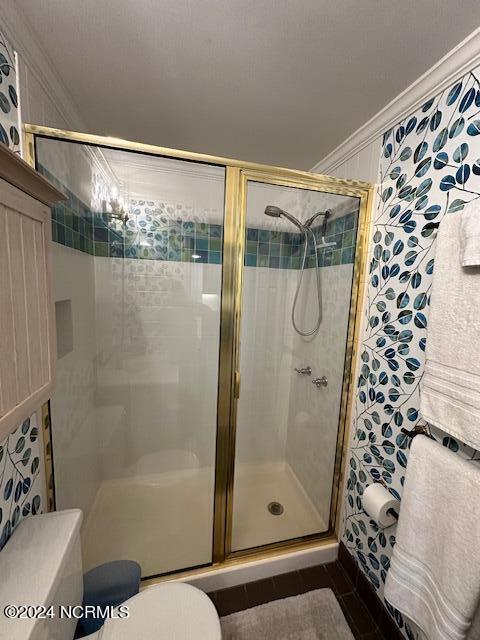 bathroom with toilet, ornamental molding, and a shower with shower door