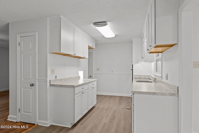 kitchen with sink, white cabinets, light hardwood / wood-style floors, and a textured ceiling