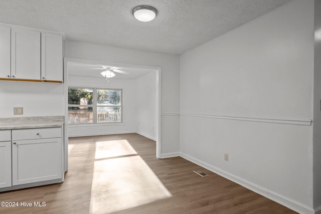 unfurnished dining area featuring ceiling fan, light hardwood / wood-style flooring, and a textured ceiling