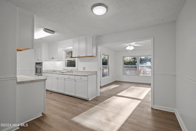 kitchen with white cabinets, a textured ceiling, light hardwood / wood-style floors, and stainless steel oven