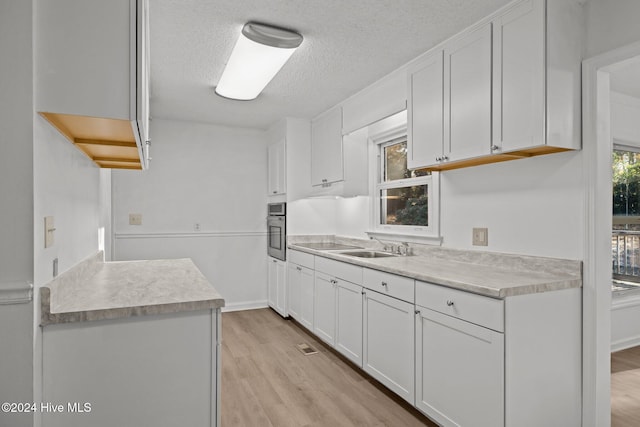 kitchen with stainless steel oven, white cabinets, sink, a textured ceiling, and light hardwood / wood-style floors