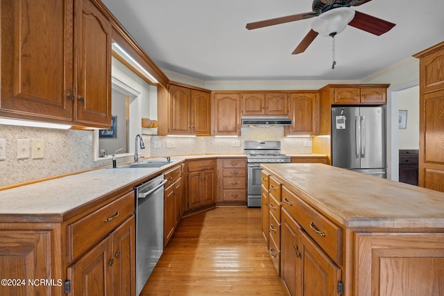 kitchen featuring appliances with stainless steel finishes, decorative backsplash, light wood-type flooring, a center island, and ceiling fan