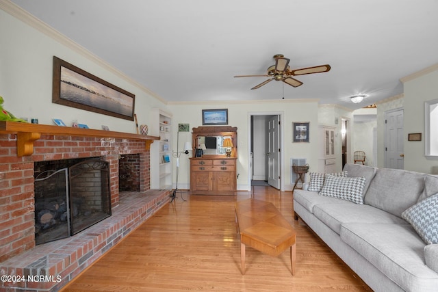 living room featuring wood-type flooring, a brick fireplace, ornamental molding, and ceiling fan