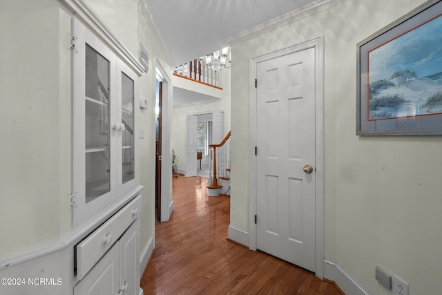 hall with wood-type flooring, crown molding, and an inviting chandelier