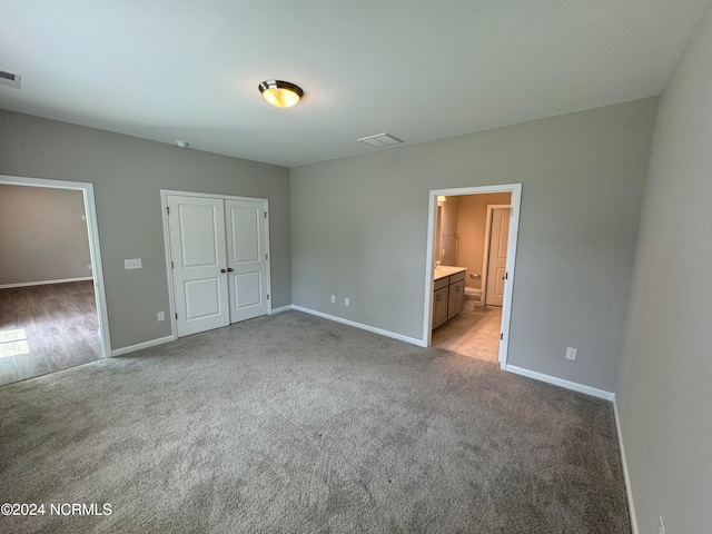 unfurnished bedroom with light colored carpet, a closet, and ensuite bath