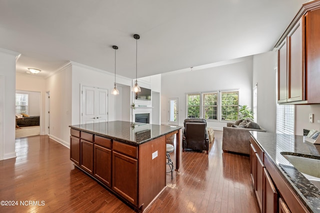 kitchen with a kitchen bar, dark hardwood / wood-style flooring, hanging light fixtures, dark stone counters, and a center island