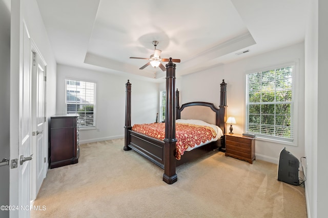 bedroom featuring a raised ceiling, light colored carpet, and ceiling fan