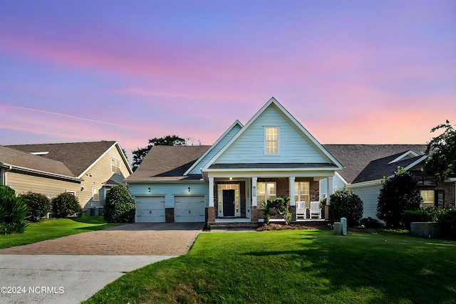 craftsman-style house with decorative driveway, an attached garage, a front yard, brick siding, and covered porch