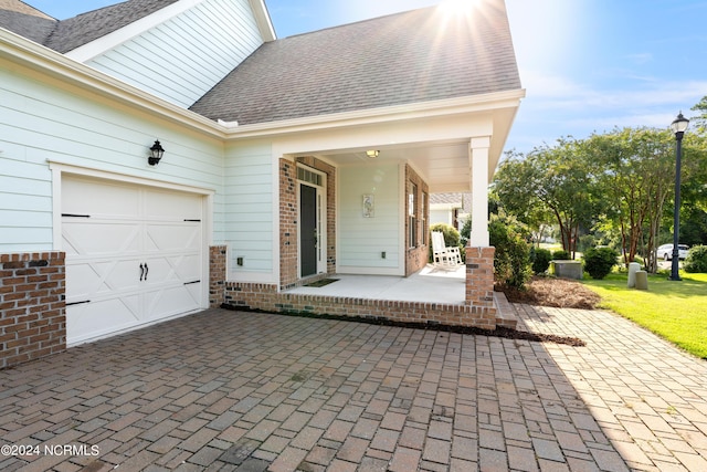 view of patio with an attached garage, a porch, and decorative driveway