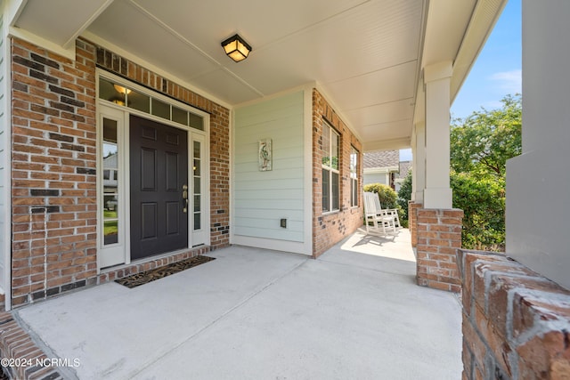 doorway to property featuring covered porch and brick siding