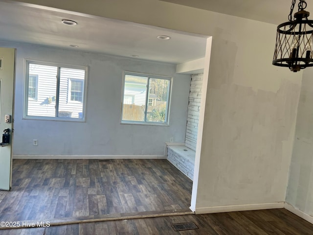 empty room with dark wood-style floors, an inviting chandelier, visible vents, and baseboards