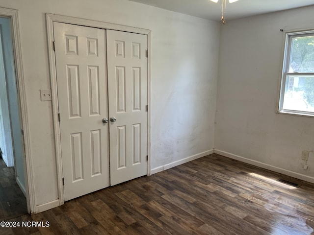 unfurnished bedroom featuring dark wood-style floors, a closet, visible vents, and baseboards