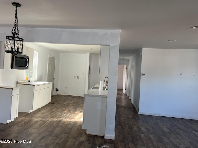 kitchen with dark wood-style flooring, light countertops, stainless steel microwave, white cabinetry, and a sink