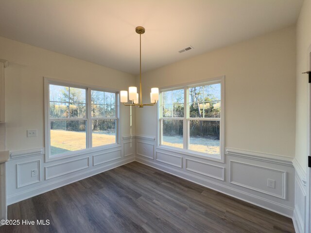 unfurnished dining area with plenty of natural light, dark hardwood / wood-style flooring, and a notable chandelier