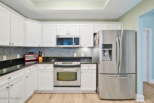 kitchen featuring dark stone countertops, light wood-type flooring, appliances with stainless steel finishes, white cabinetry, and tasteful backsplash