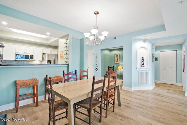 dining space featuring light hardwood / wood-style flooring, a raised ceiling, and a chandelier