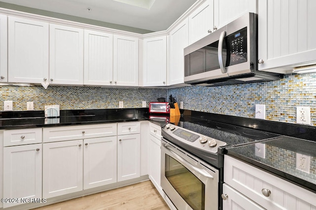 kitchen featuring white cabinets, light hardwood / wood-style flooring, appliances with stainless steel finishes, dark stone counters, and decorative backsplash