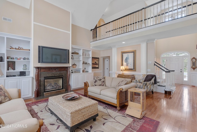 living area featuring high vaulted ceiling, a high end fireplace, visible vents, built in features, and light wood finished floors