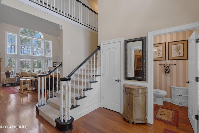 staircase featuring baseboards, hardwood / wood-style floors, a towering ceiling, and wallpapered walls