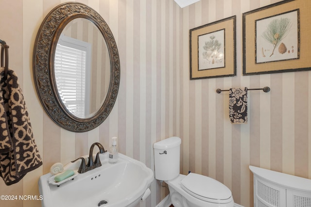 half bath featuring a sink, toilet, and wallpapered walls