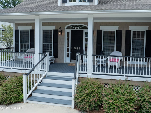 entrance to property with a porch and roof with shingles