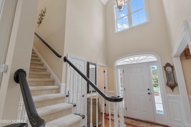 foyer entrance with a high ceiling, stairway, wood finished floors, and wainscoting