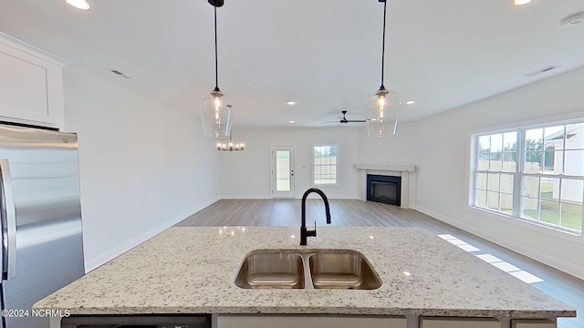 kitchen featuring open floor plan, freestanding refrigerator, hanging light fixtures, light stone countertops, and a kitchen island with sink