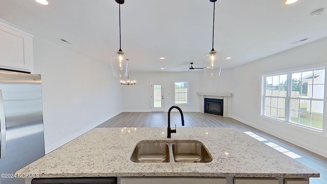 kitchen with freestanding refrigerator, a kitchen island with sink, decorative light fixtures, and light stone countertops