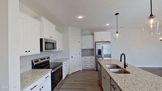 kitchen with light stone counters, decorative light fixtures, appliances with stainless steel finishes, white cabinets, and a sink