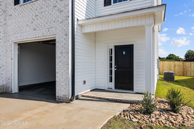 view of exterior entry with concrete driveway and fence