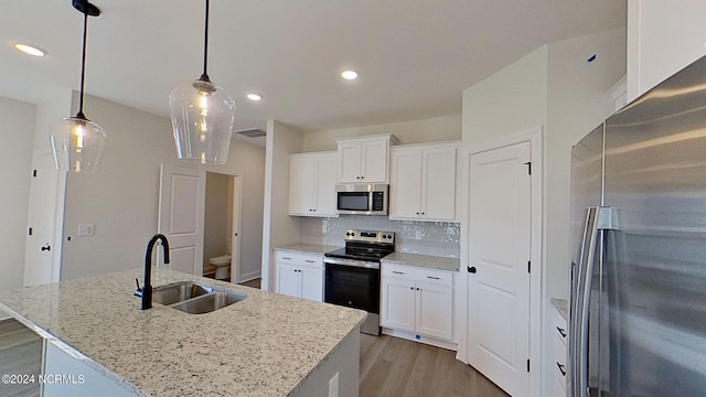 kitchen featuring stainless steel appliances, hanging light fixtures, a kitchen island with sink, white cabinetry, and a sink