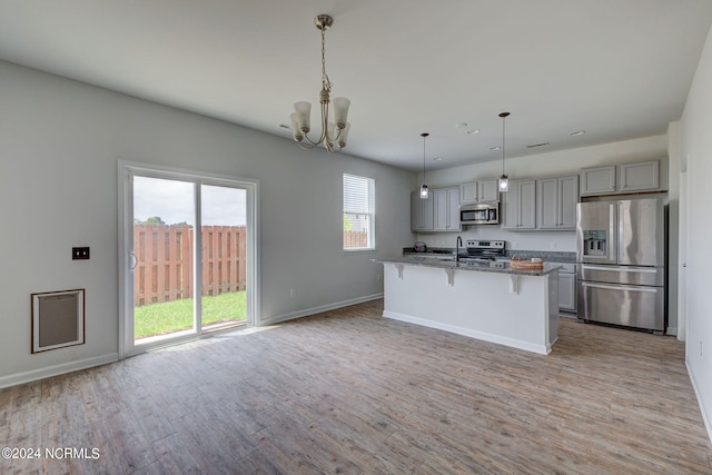 kitchen with decorative light fixtures, a kitchen bar, a center island with sink, light hardwood / wood-style floors, and appliances with stainless steel finishes