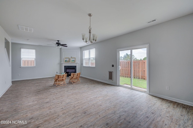 unfurnished living room featuring plenty of natural light, ceiling fan with notable chandelier, and wood-type flooring