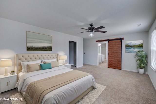 carpeted bedroom with ensuite bath, a barn door, and ceiling fan