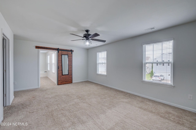 interior space featuring a healthy amount of sunlight, light colored carpet, a barn door, and ceiling fan