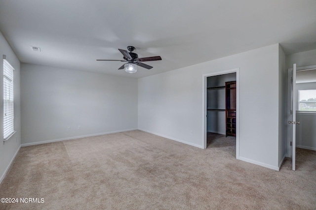 unfurnished bedroom featuring a closet, light carpet, a walk in closet, and ceiling fan