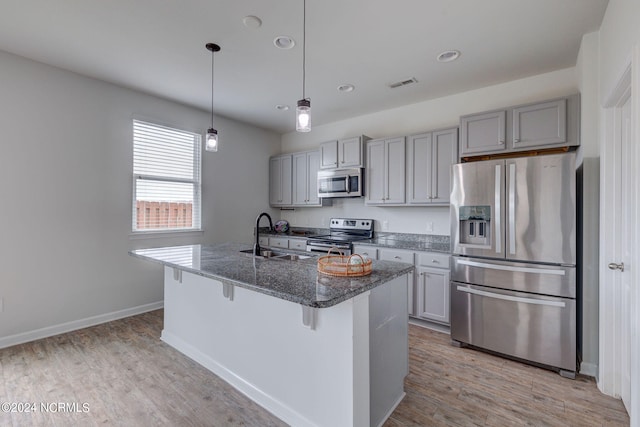 kitchen with light hardwood / wood-style flooring, stainless steel appliances, hanging light fixtures, sink, and a center island with sink