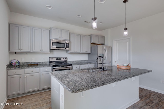 kitchen with hardwood / wood-style flooring, stainless steel appliances, hanging light fixtures, sink, and a kitchen island with sink