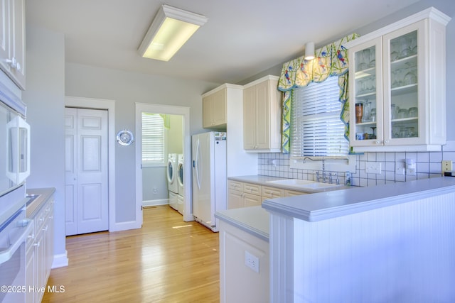 kitchen with tasteful backsplash, glass insert cabinets, washer and dryer, white fridge with ice dispenser, and a sink