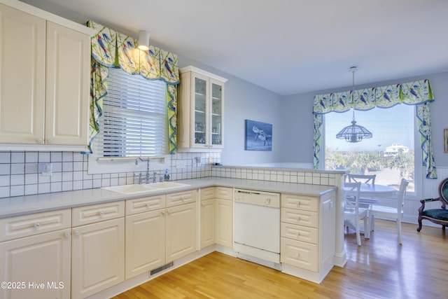 kitchen featuring visible vents, a peninsula, white dishwasher, light countertops, and a sink