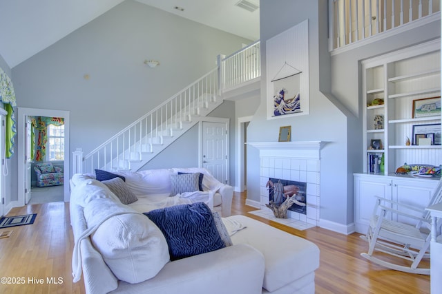 living area featuring built in shelves, wood finished floors, high vaulted ceiling, a tile fireplace, and stairs