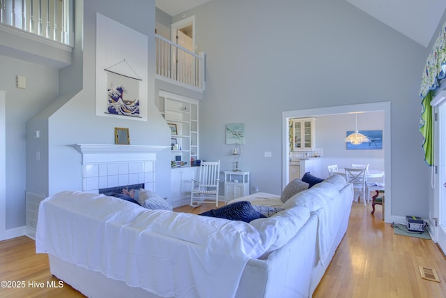 living room featuring high vaulted ceiling, a fireplace, visible vents, and wood finished floors