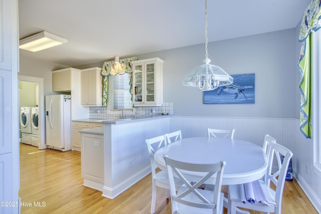 kitchen featuring a wainscoted wall, light wood-style floors, washer and dryer, light countertops, and white fridge with ice dispenser