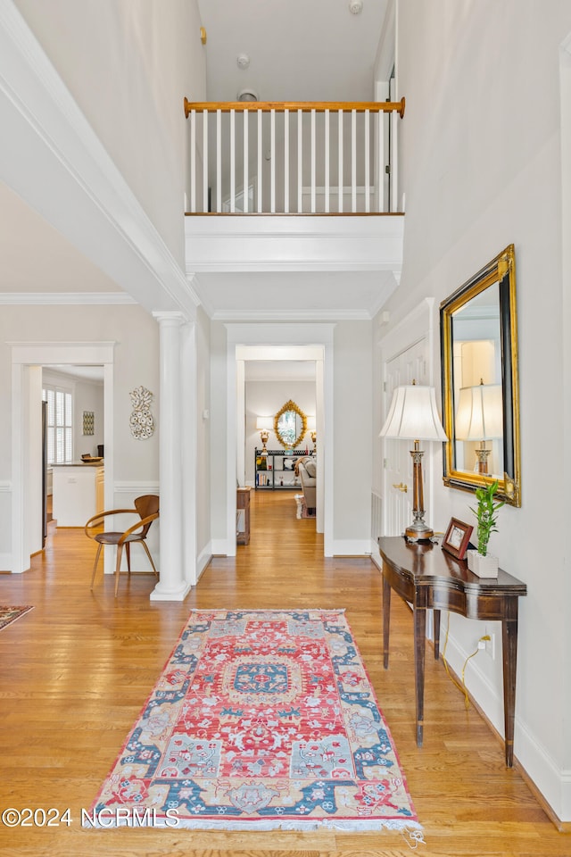 foyer entrance featuring a towering ceiling, light wood-type flooring, and ornate columns